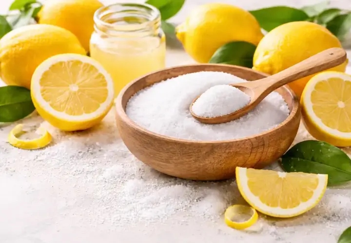 Cytryny i miska z białym proszkiem, przypominającym sól. Warto pamiętać o potencjalnej citric acid szkodliwość przy nadmiernym spożyciu.