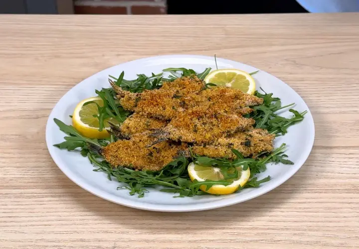 Piatto di alici al forno croccanti, servite su un letto di rucola fresca e guarnite con spicchi di limone.