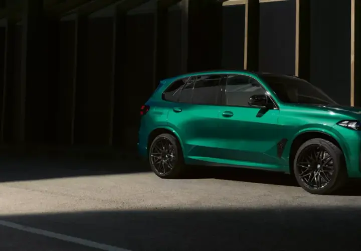 Zielony BMW X5 M z czarnymi felgami stoi na tle ciemnej architektury, oświetlony pasem światła.