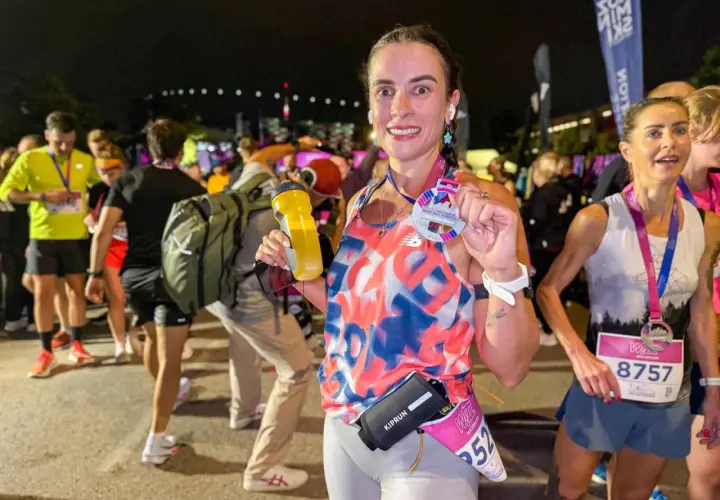 Uśmiechnięta biegaczka po ukończeniu biegu na 100 km, trzymająca medal i bidon.
