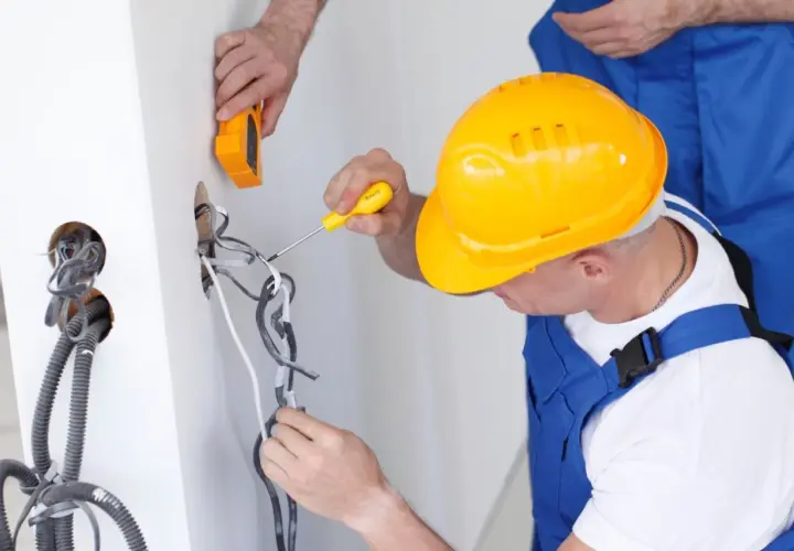 Elektryk w żółtym kasku pracuje przy instalacji, zastanawiając się, ile zarabia elektryk w Norwegii.