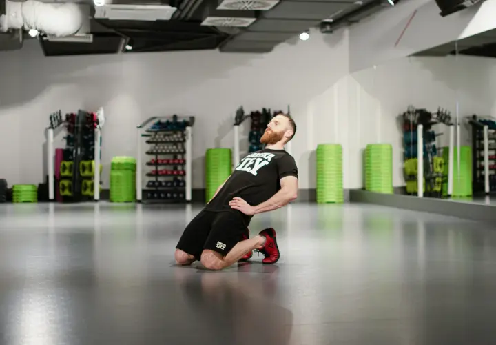 Mężczyzna wykonuje ćwiczenie nordic curl, klęcząc na podłodze i pochylając się do przodu.