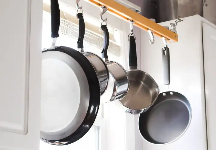Une astuce rangement casserolier : des poêles suspendues à une barre en bois, libérant de l'espace dans les placards.
