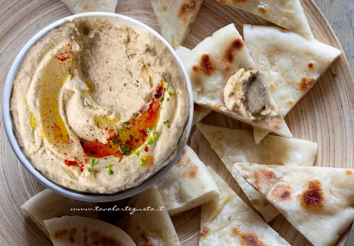 Ciotola di hummus di lenticchie con olio, paprika e prezzemolo, servito con pane pita tagliato a spicchi.