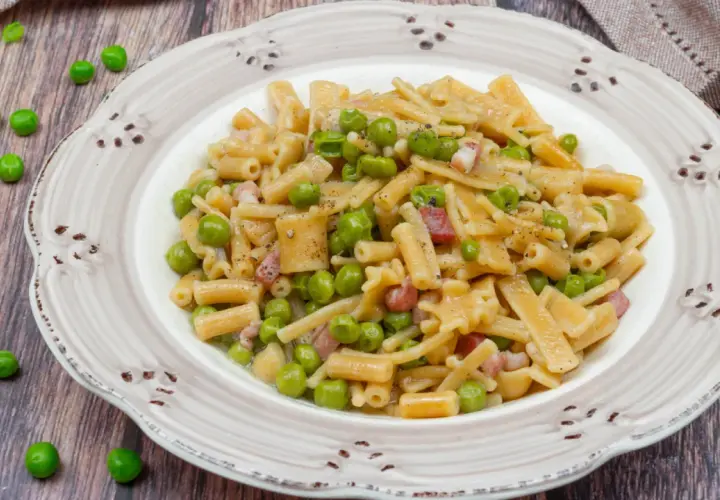 Un piatto di pasta con piselli, pancetta e pepe nero, servito su un piatto rustico.