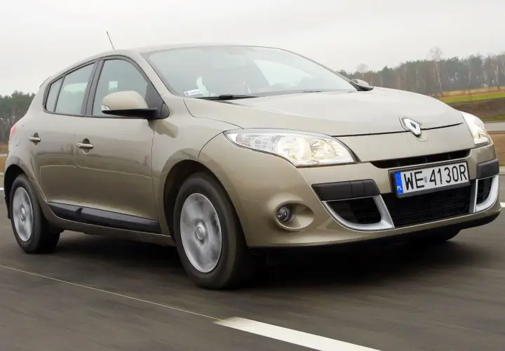Złoty Megane 3 w ruchu drogowym, z widocznymi światłami i tablicą rejestracyjną WE 4130R.