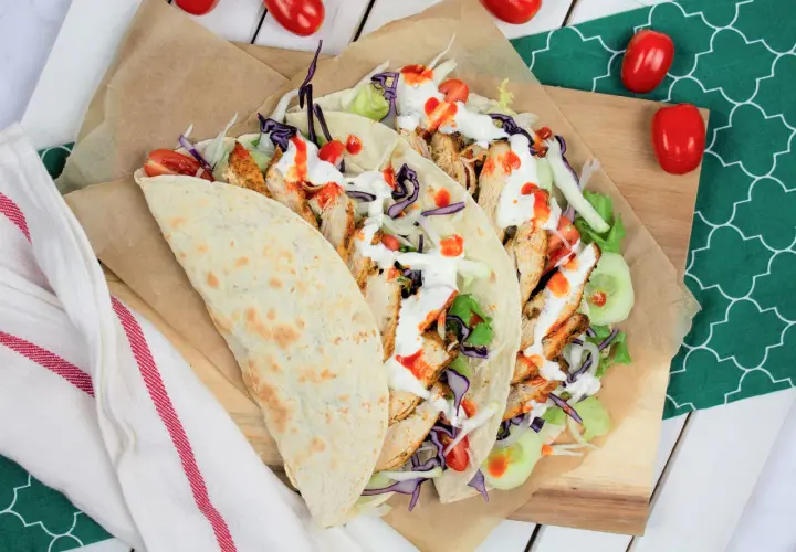 Kebab w tortilli z kurczakiem, warzywami i sosami, obok pomidorki.