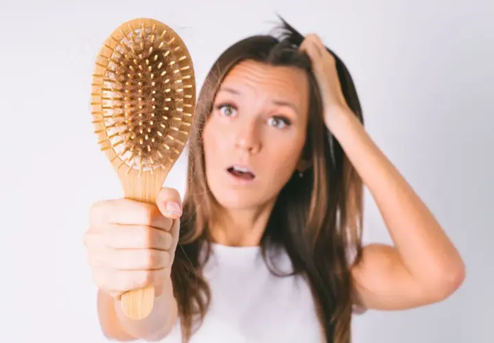 Mujer preocupada por la caída de pelo postparto, mostrando un cepillo con cabello.