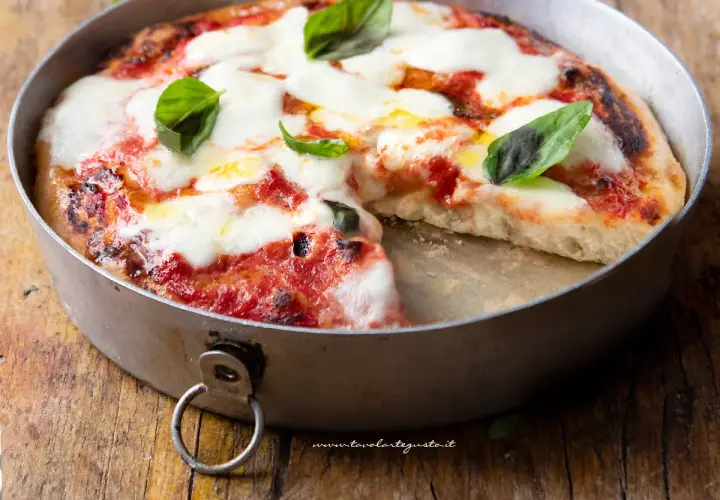 Pizza margherita appena sfornata in friggitrice ad aria, con mozzarella filante e basilico fresco su un tagliere di legno.