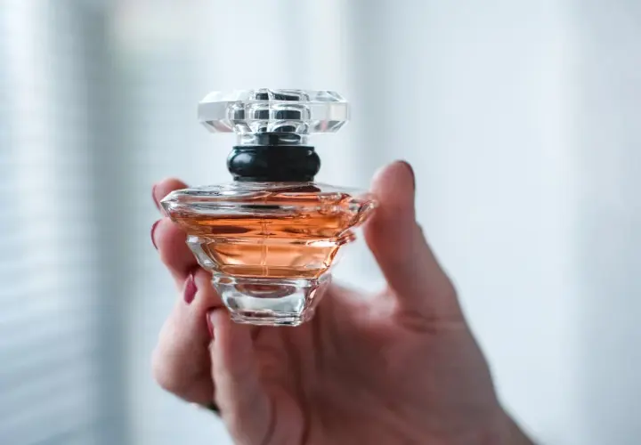 Dłoń trzyma flakonik perfum o bursztynowym kolorze, przypominający Baccarat Rouge.