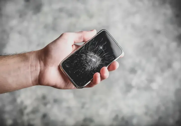 Dłoń trzyma pęknięty telefon. Zastanawiasz się, ile trwa wymiana szybki w telefonie?