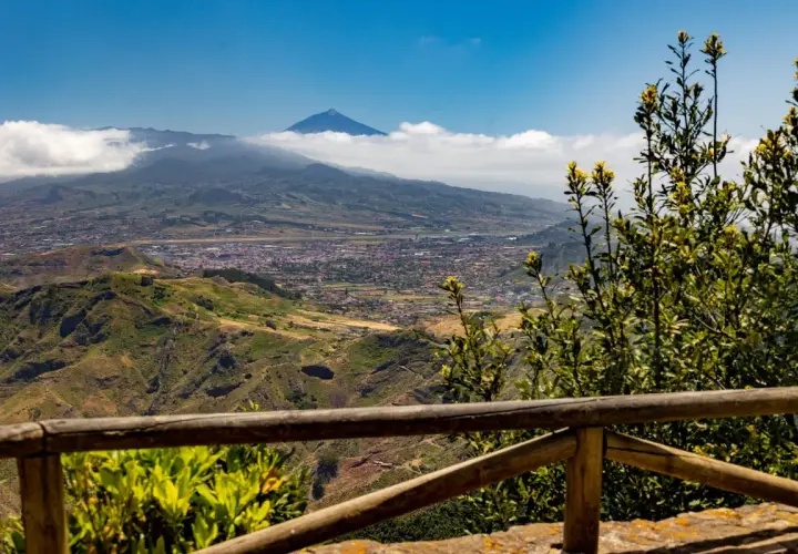 Vista panorámica desde Anaga, Tenerife, con el Teide asomando entre las nubes. Un paisaje verde y montañoso se extiende hasta el mar.