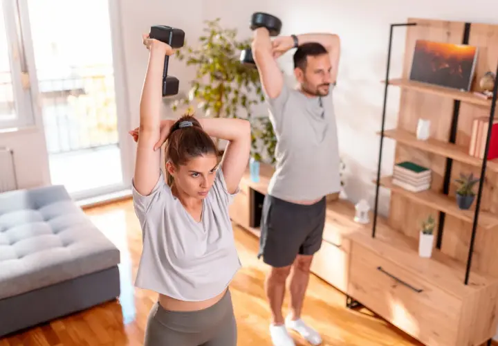 Para ćwiczy ćwiczenia na triceps w domu, podnosząc hantle nad głowę.