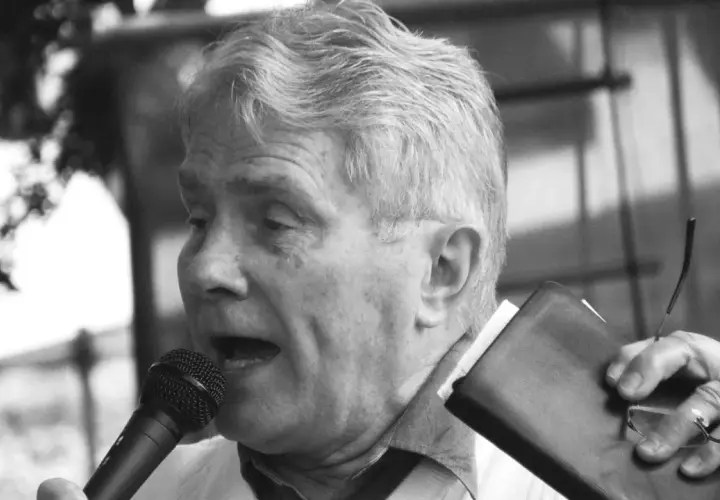 Luis Palau spricht ins Mikrofon, hält eine Bibel und eine Brille.