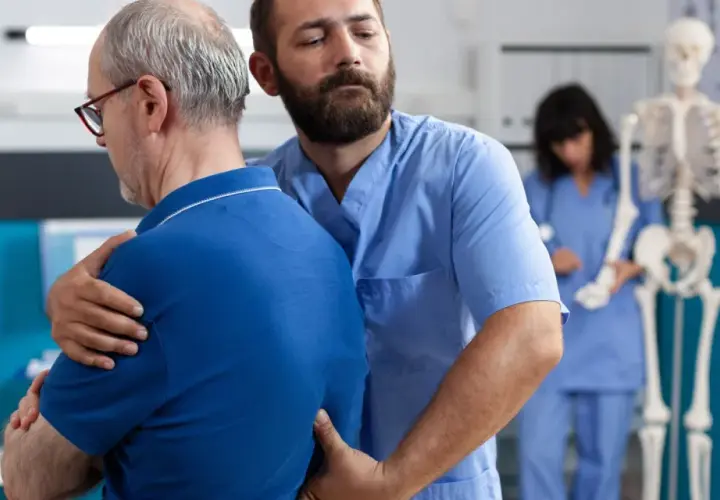 Fizjoterapeuta pomaga pacjentowi z bólem pleców i mięśni. W tle szkielet i pielęgniarka.