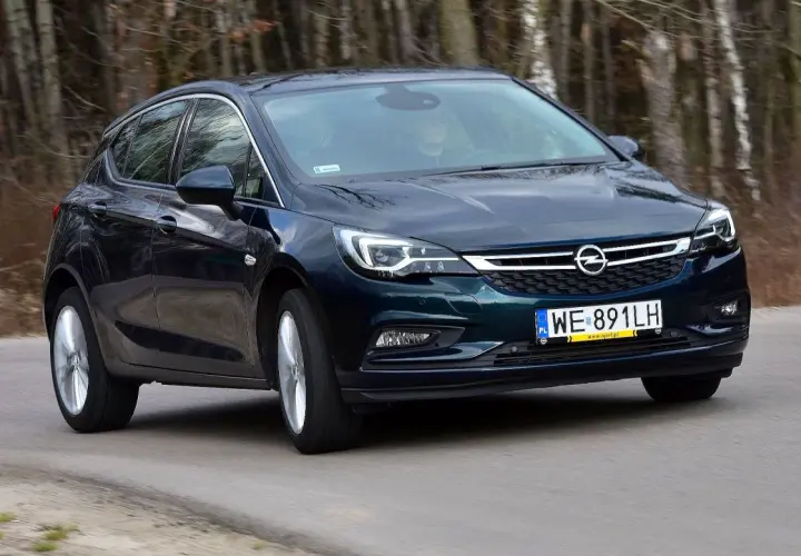 Ciemnozielony Opel Astra K 1.4 Turbo jedzie po drodze wśród drzew.