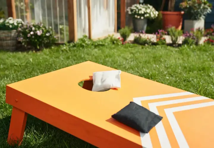 Orange Cornhole-Brett mit weißen Streifen, bereit für das Spiel. Perfekt für das **cornhole selber bauen** im Garten.