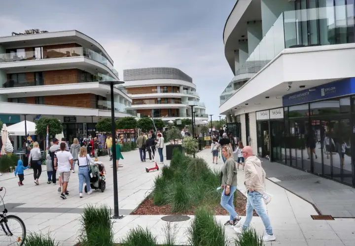 Spacer po nowoczesnej promenadzie w Świnoujściu, gdzie liczne atrakcje czekają na turystów. Ludzie spacerują, sklepy i apartamenty zachwycają architekturą.