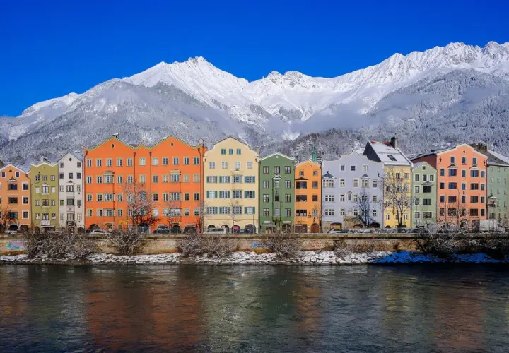 Kolorowe kamienice nad rzeką, w tle ośnieżone góry. To piękne Innsbruck atrakcje, które warto zobaczyć zimą.