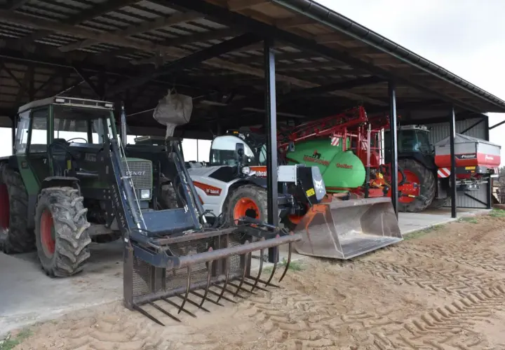 Ciągniki i maszyny rolnicze pod zadaszeniem. Widać zielony Fendt z ładowaczem, biały Bobcat, zielony opryskiwacz i ciągnik z rozsiewaczem. To wszystko w budynku gospodarczym bez zgłoszenia.