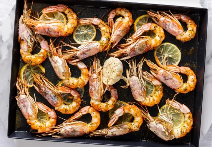 Gamberoni al forno dorati e succulenti, conditi con erbe aromatiche e fette di limone, pronti per essere gustati.