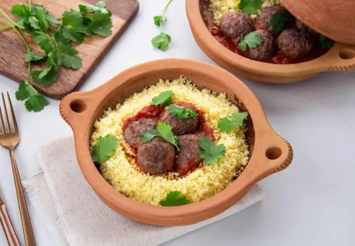 Délicieuse recette de boulette de boeuf haché avec sauce, servie sur un lit de couscous et garnie de coriandre fraîche.