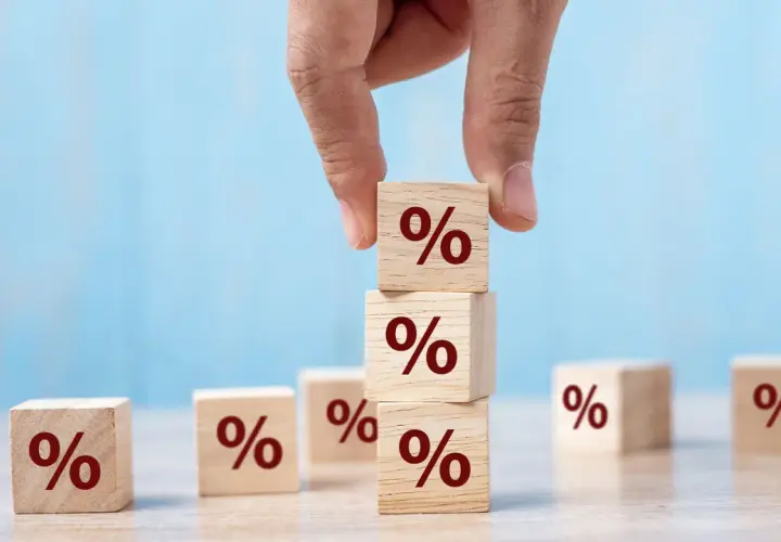 Main d'une personne empilant des cubes en bois marqués du symbole "%", symbolisant le calcul du taux de remplacement retraite.
