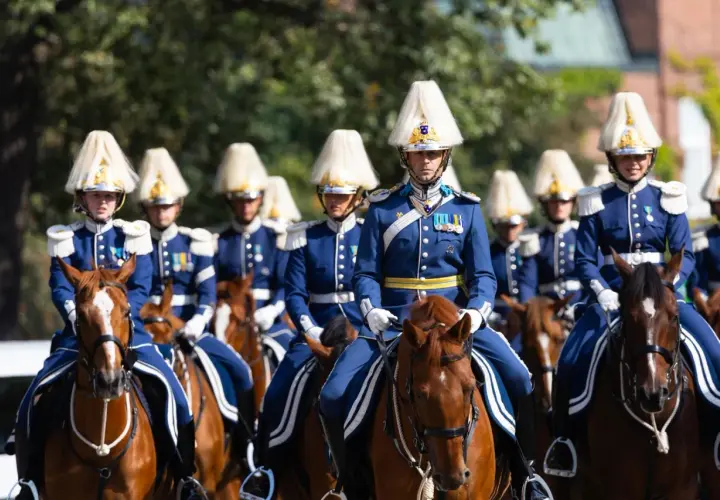 Livgardet i sina blå uniformer och höga hattar rider på bruna hästar.