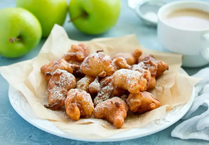 Montón de buñuelos de manzana dorados y espolvoreados con azúcar glas, listos para disfrutar.