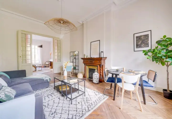 Salon lumineux avec canapé gris, tapis graphique, cheminée ancienne et table à manger. Une belle idée home staging pour un espace convivial.