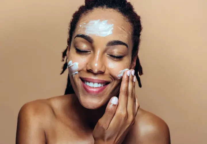 Une femme applique une crème sur son visage, une étape essentielle de sa routine de protection contre le soleil.