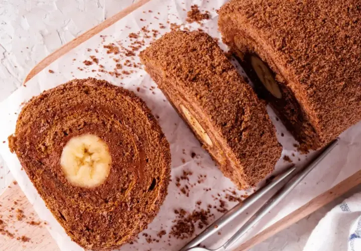 Czekoladowe ciasto gąbka z bananem w środku, pokrojone na plastry, posypane wiórkami.