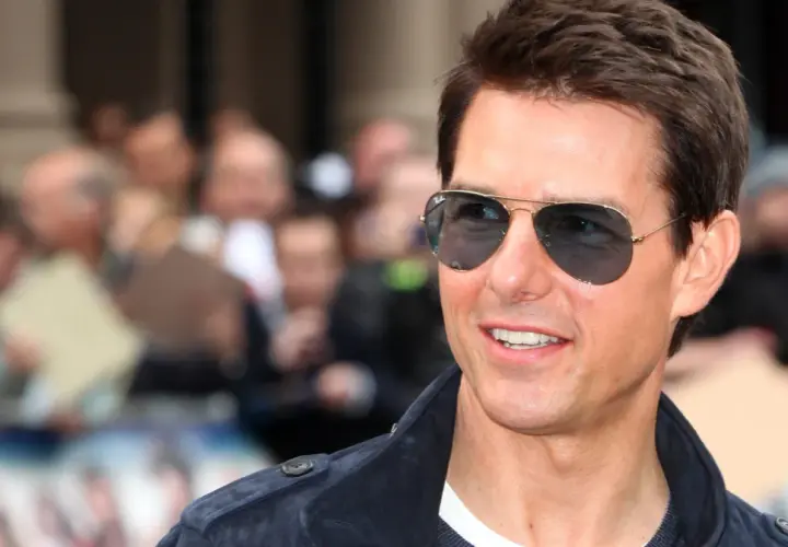 Tom Cruise w okularach przeciwsłonecznych, uśmiechnięty, na tle tłumu. Wygląda jakby właśnie świętował swoje urodziny, kiedy urodził się Tom Cruise.