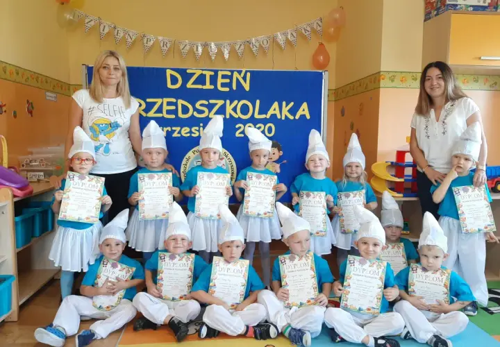 Dzieci w strojach smerfów z dyplomami, z nauczycielkami w tle.