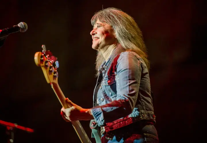 Suzi Quatro obecnie, z uśmiechem na twarzy, gra na gitarze basowej w dżinsowej kurtce.