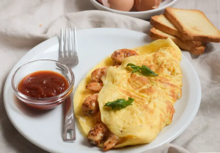 Tortilla de gambas dorada y jugosa, servida con salsa y tostadas. Un desayuno perfecto.