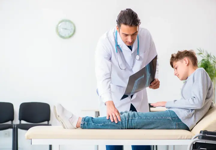 Arzt erklärt Röntgenbild einem Jungen, der auf einer Liege sitzt. Möglicherweise geht es um Orthese Druckstellen.