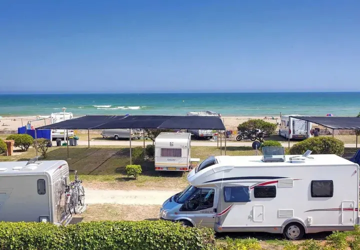 Autocaravanas y caravanas en un camping junto al mar, ideal para camping en Barcelona. El mar azul y la playa invitan a disfrutar del sol.