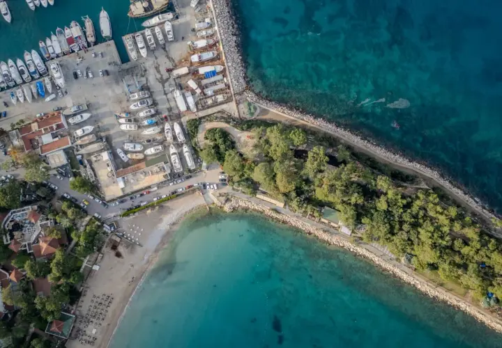 Widok z lotu ptaka na port i plażę w Kemerze, Turcja. Widać liczne jachty, łodzie, budynki i zielone tereny. To idealne miejsce na odkrywanie atrakcji Kemer.