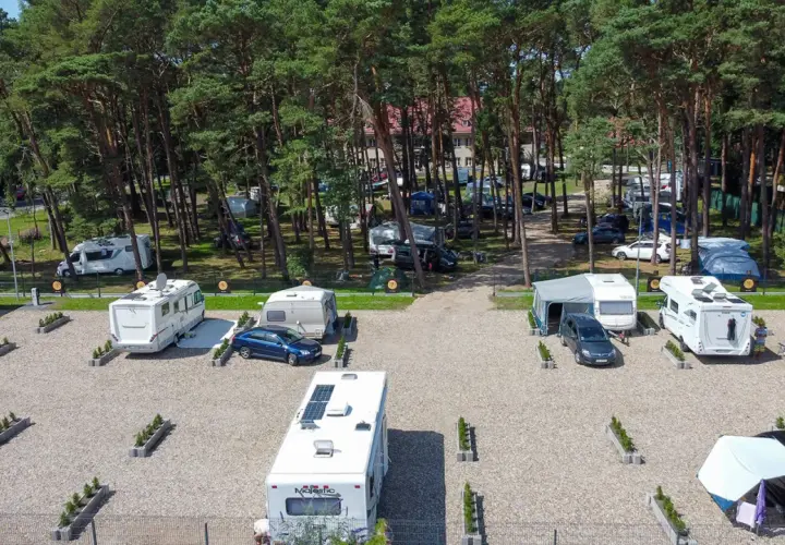 Kampery i przyczepy kempingowe na żwirowym polu namiotowym w lesie sosnowym. Widok z lotu ptaka na sea camp Rogowo.