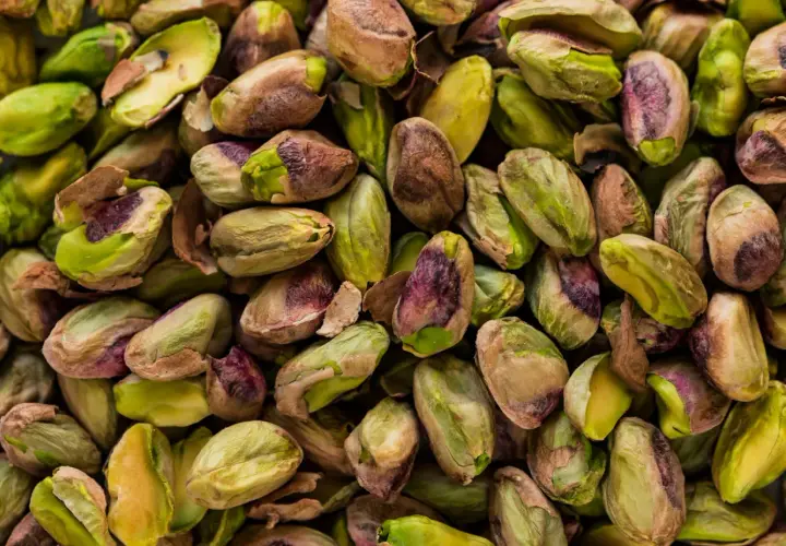 Zbliżenie na stos łuskanych pistacji, niektóre z zielonymi nasionami, inne z brązowymi łupinami.