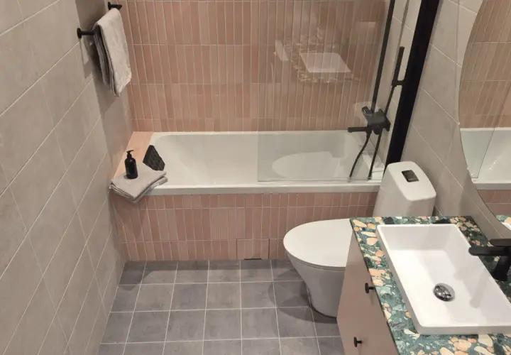 Ett modernt badrum med rosa kakel bakom badkaret och en handfatskommod i terrazzo.