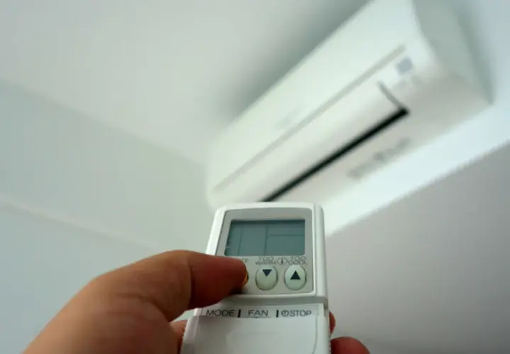Mano sujetando un control remoto de aire acondicionado, ajustando la temperatura para controlar cuanto gasta un aire acondicionado.