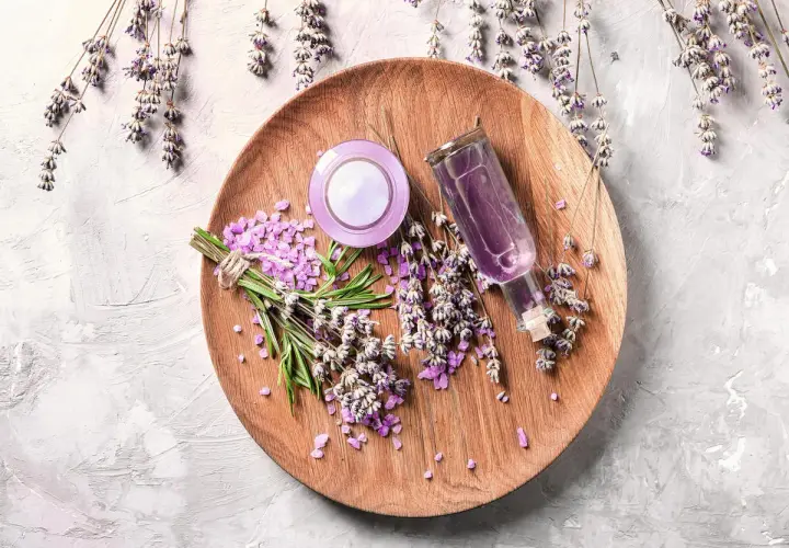 Sur un plateau en bois, des brins de lavande fraîche et séchée, des cristaux violets et une petite bouteille de liquide pour faire bouillir de la lavande.