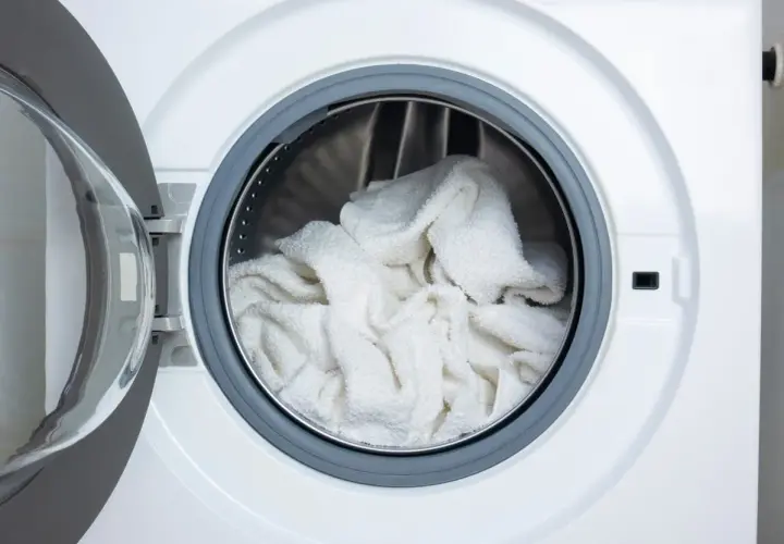 Tambour de machine à laver rempli de linge blanc prêt pour un lavage éclatant avec de l'eau de javel pour blanchir le linge en machine.