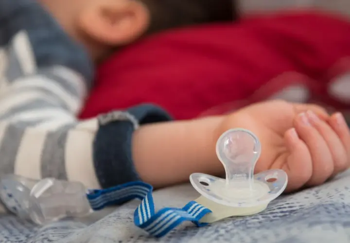 Dziecko śpi z rączką obok smoczka, który może powodować odparzenia.