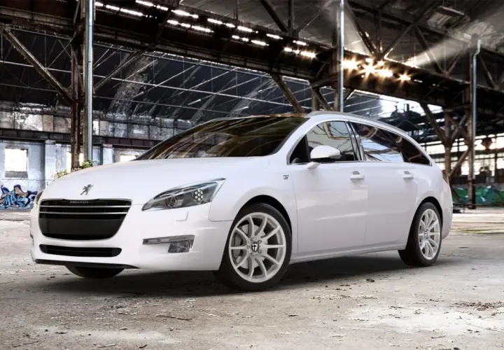 Biały Peugeot 508 SW na jasnych felgach, z widocznym rozmiarem opon, stoi w opuszczonej hali przemysłowej.