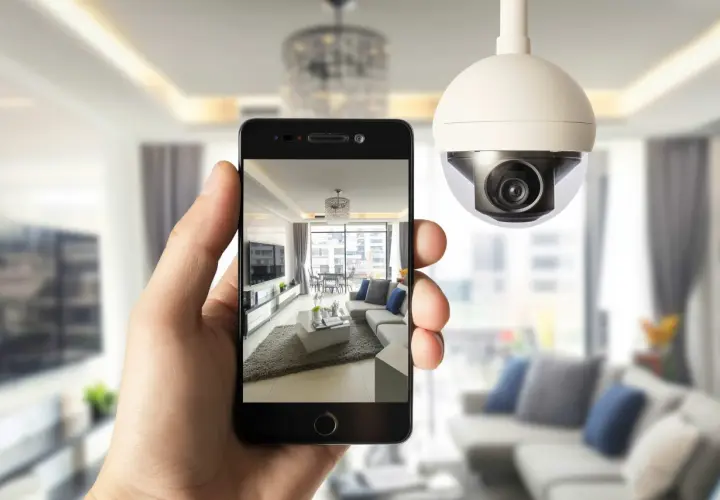 Una mano sostiene un teléfono que muestra una sala de estar moderna, mientras una cámara de seguridad wdr vigila el espacio.