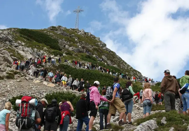 Tłum turystów na skalistej trasie na Giewont. W oddali widoczny krzyż.