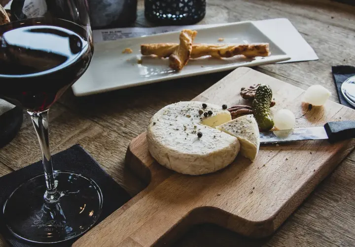 Verre de vin rouge avec un plateau de fromage, cornichons et noix. Un délice pour accompagner une dégustation de vin rouge avec charcuterie et fromage.